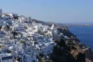 View of whitewashed houses with blue domes in Santorini, Greece, overlooking the Aegean Sea at sunset