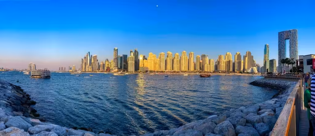 View from Bluewaters Island of the Dubai JBR skyline, featuring modern high-rises, the beach, and the Arabian Gulf in the foreground.