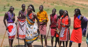 Dancing men in traditional Kenyan clothing performing a cultural dance outdoors