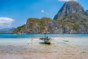 Traditional Filipino banca boat anchored in shallow turquoise water with limestone cliffs in Palawan, Philippines