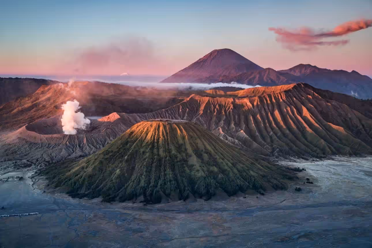 Volcanic landscape with smoking crater and mountains at sunrise in Indonesia