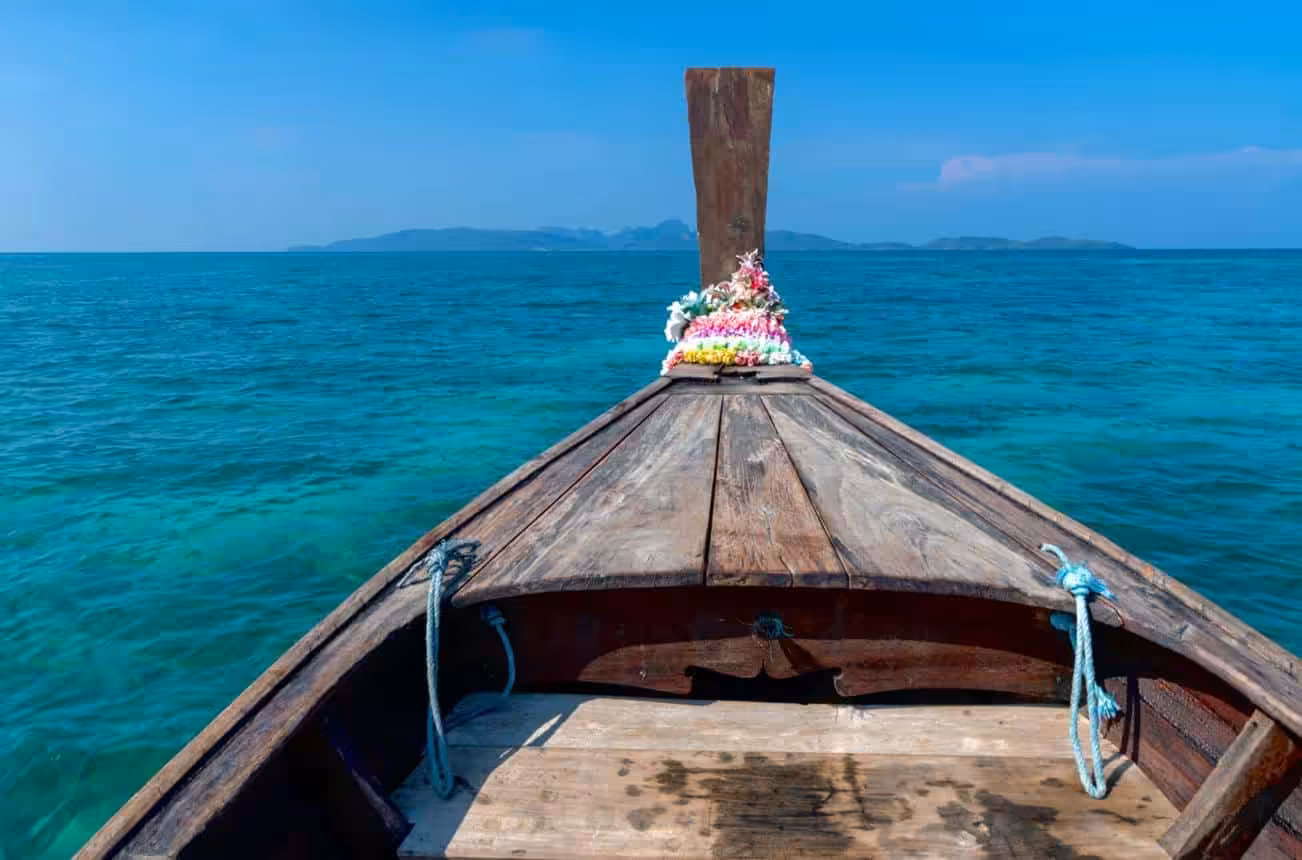 Traditional wooden boat sailing on clear turquoise sea toward tropical islands