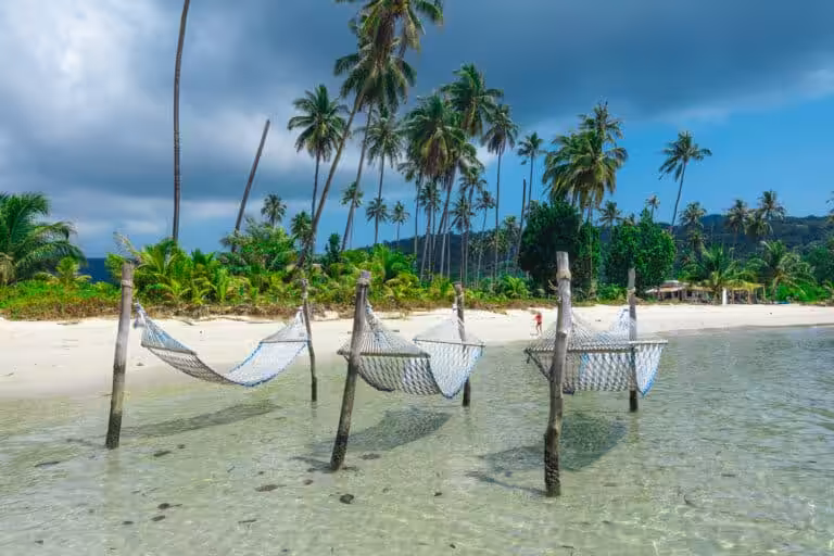 Hammocks over shallow clear water on tropical beach with palm trees in the Philippines