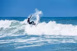Surfer riding a powerful ocean wave with water spray under a clear blue sky