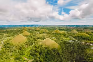 Alt Text Aerial drone view of the iconic Chocolate Hills – hundreds of perfectly cone-shaped grass-covered limestone hills stretching to the horizon across a lush green tropical landscape in Bohol, Philippines