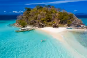Aerial view of a small tropical island with a white sand beach, traditional bangka boat and a kayaker in crystal-clear turquoise water in Coron, Palawan, Philippines