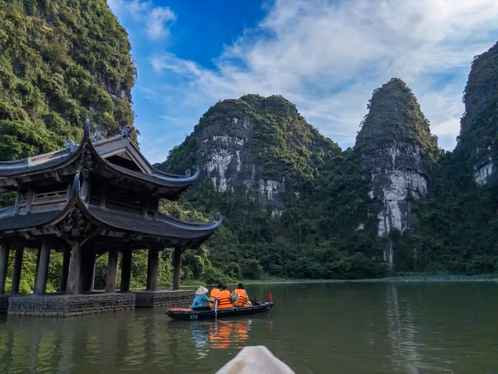 Rowing boat passing a temple pavilion beneath limestone karsts on a Trang An boat tour, Vietnam