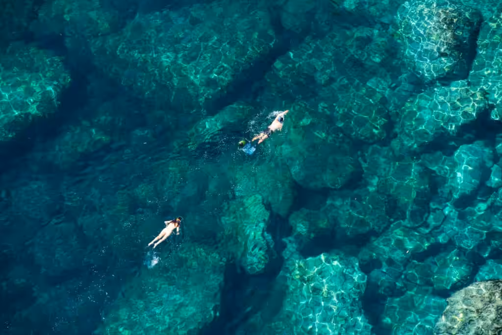 Aerial view of two people snorkeling over a coral reef in clear turquoise water