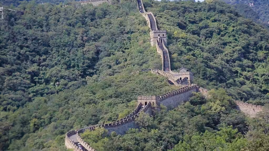 Aerial view of the Great Wall of China winding through dense green summer forest over steep mountain ridges at the Mutianyu section, Beijing, China