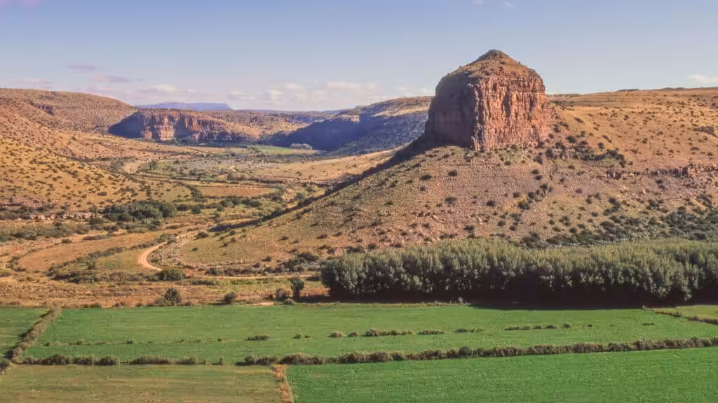 A dramatic Karoo valley near Nieu-Bethesda with a solitary sandstone butte, green irrigated farmland, a winding dirt road and arid canyon landscape stretching to the horizon, Eastern Cape, South Africa